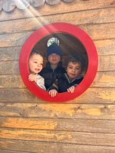 Three children smiling through a round window.