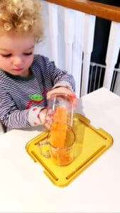 Child pouring orange substance into glass.